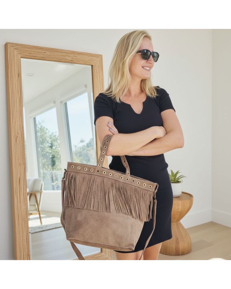 Cabas en daim taupe avec franges et œillets dorés, porté à l'épaule