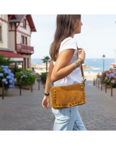 Femme portant un sac en daim en bandoulière camel, look bohème chic avec jean et t-shirt blanc, accessoire mode tendance 2025