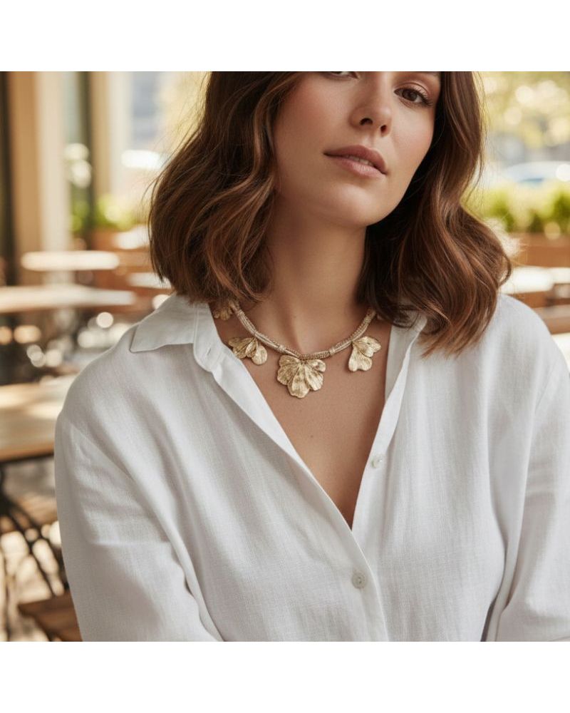 Collier doré avec cordon tressé, chaîne mêlée et breloques feuilles sur un modèle portant une chemise blanche