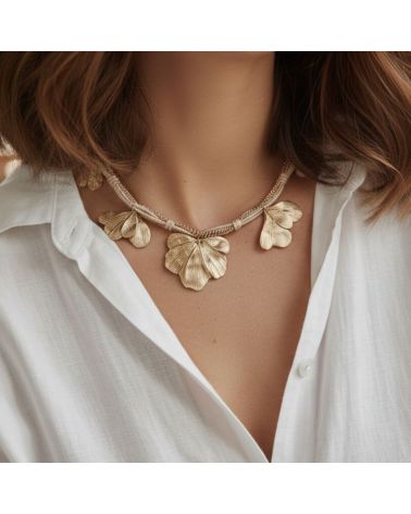 Collier doré Mile mila avec cordon tressé, chaîne mêlée et breloques feuilles sur un modèle portant une chemise blanche