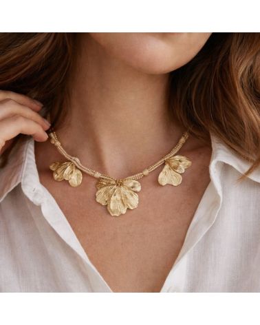 Collier doré Mile mila avec cordon tressé, chaîne mêlée et breloques feuilles sur un modèle portant une chemise blanche