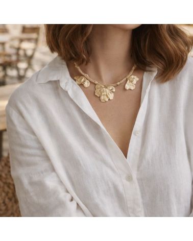 Collier doré Mile mila avec cordon tressé, chaîne mêlée et breloques feuilles sur un modèle portant une chemise blanche
