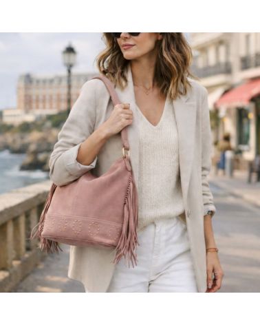 Femme style effortless chic portant le sac Lucile rose poudré à franges en daim, porté épaule, dans une rue de Biarritz