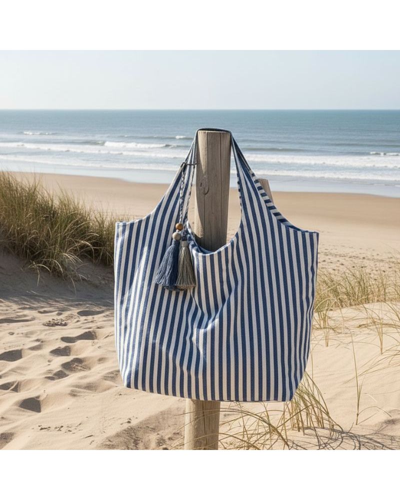 Sac de plage rayé bleu et blanc Marinella en coton grand format avec fermeture zippée posé sur la plage face à l’océan