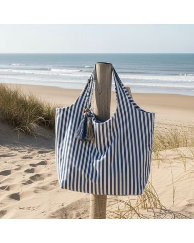 Sac de plage rayé bleu et blanc Marinella en coton grand format avec fermeture zippée posé sur la plage face à l’océan