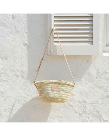 Panier en osier tressé avec bandoulière en cuir suspendu à un volet blanc