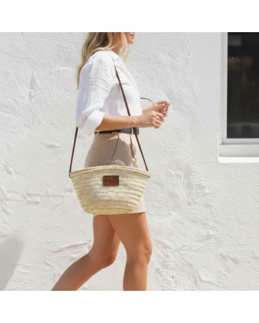 Femme marchant avec un petit panier de plage en osier et détails en cuir marron foncé style bohème chic