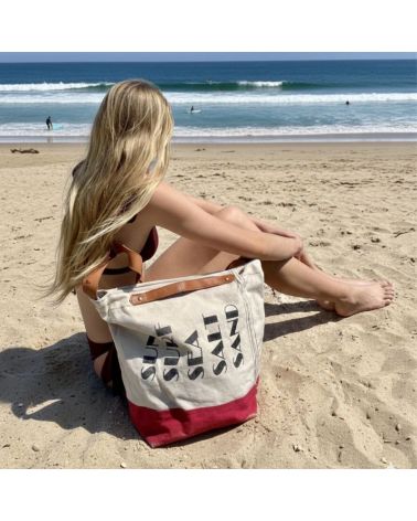 Femme assise sur le sable avec le sac de plage Chloé écru et rose fuchsia, vue sur l'océan et les vagues à Seignosse