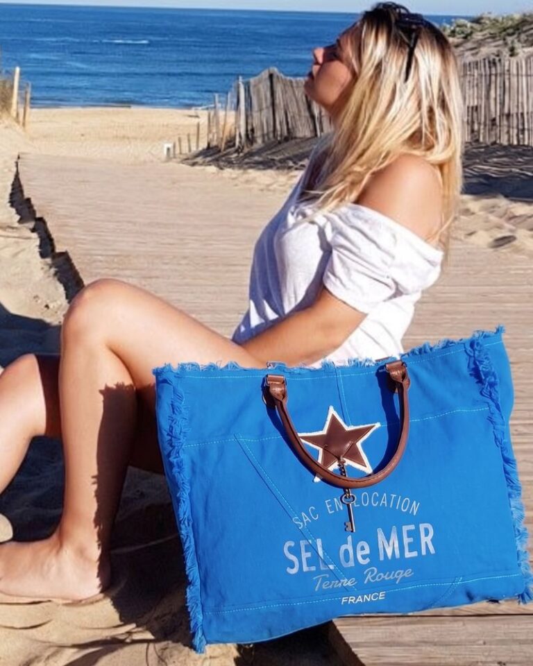 Femme assise sur une terrasse en bois à la plage avec un grand sac cabas de plage bleu roi Sel de Mer