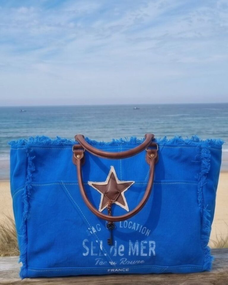 Sac de plage bleu roi XL Sel de Mer posé sur une rembarde en bois avec vue sur mer