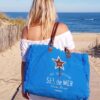 Sac de plage XL bleu roi de la collection Sel de Mer avec détail étoile et anses en cuir, porté à l'épaule sur un chemin menant à la mer