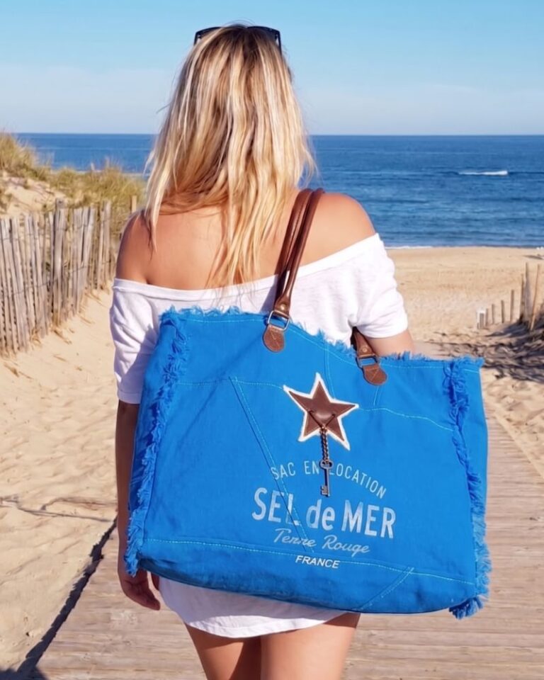 Sac de plage XL bleu roi de la collection Sel de Mer avec détail étoile et anses en cuir, porté à l'épaule sur un chemin menant à la mer