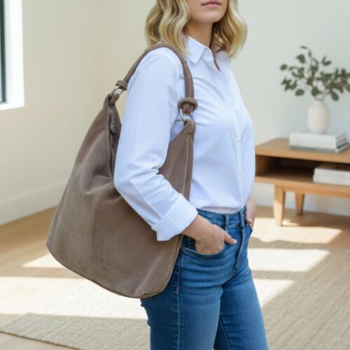 sac hobo en daim taupe porté à l’épaule avec chemise blanche, style bohème chic Sac hobo en daim taupe porté à l’épaule avec chemise blanche, style bohème chic