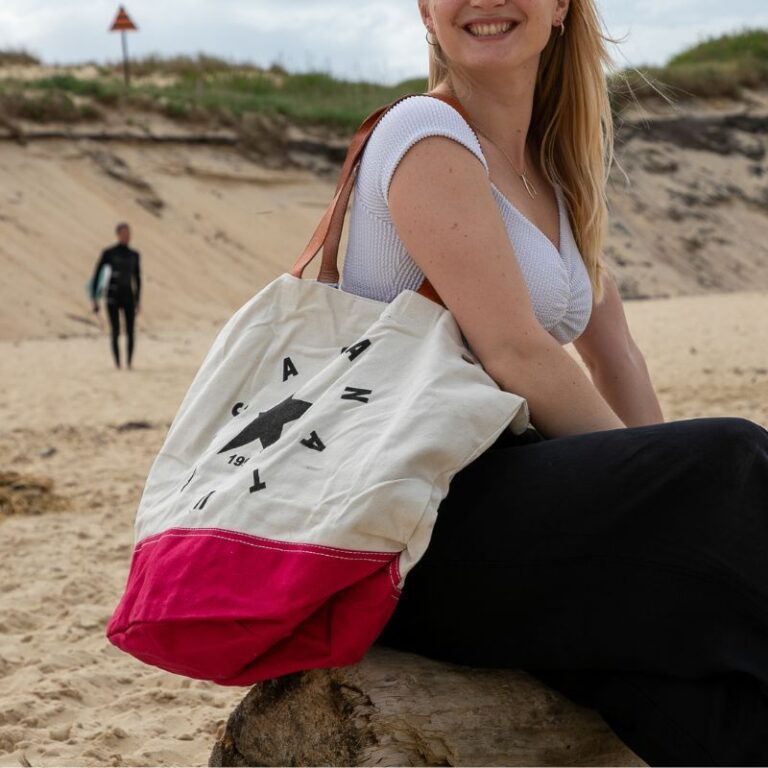 Sac de plage femme en toile écrue et rouge avec étoile noire, porté à l’épaule sur la plage face à l’océan à Seignosse