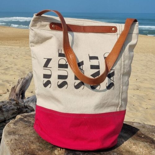 Détail du sac de plage Chloé en coton bordeaux et beige disposé sur du bois flotté, plage sauvage de Seignosse dans les Landes