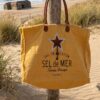 Grand sac cabas Sel de Mer en toile recyclée jaune safran suspendu à un poteau en bois sur une plage landaise. Détails en cuir et impression vintage sur le devant