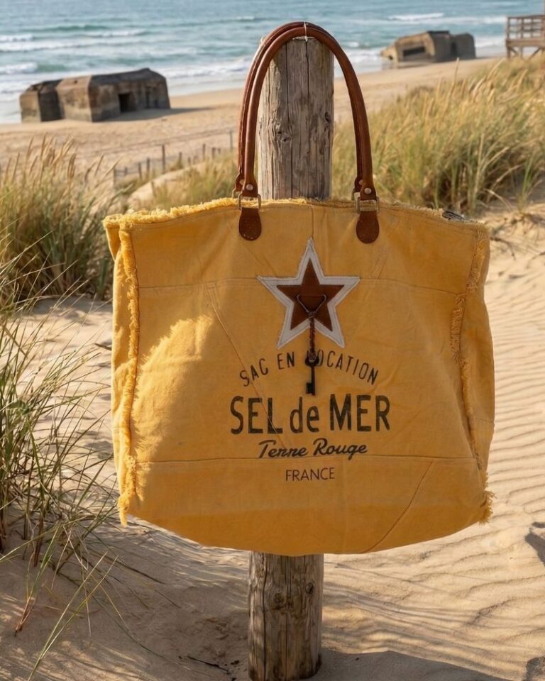 Grand sac cabas Sel de Mer en toile recyclée jaune safran suspendu à un poteau en bois sur une plage landaise. Détails en cuir et impression vintage sur le devant
