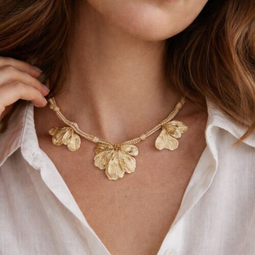 Collier doré Mile mila avec cordon tressé, chaîne mêlée et breloques feuilles sur un modèle portant une chemise blanche