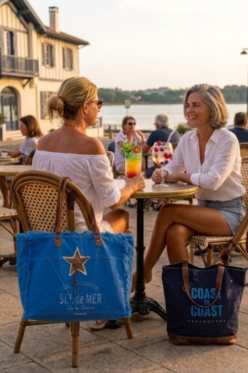 Deux femmes sur une terrasse de café à Hossegor avec leurs sacs de plage en toile recyclée Zosha Collection au coucher du soleil